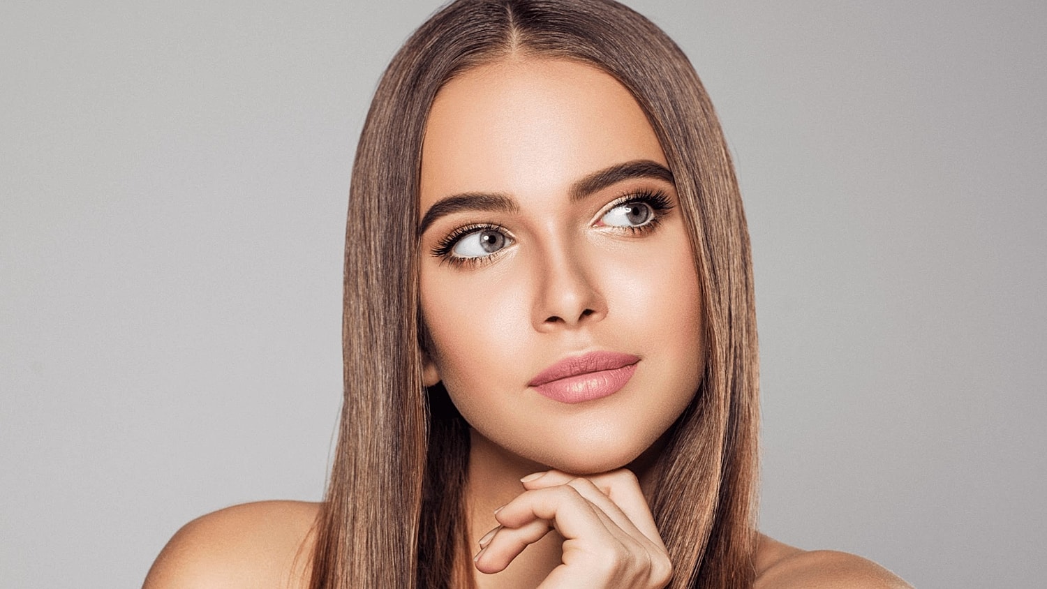 Woman with long hair, thoughtful expression, neutral background.