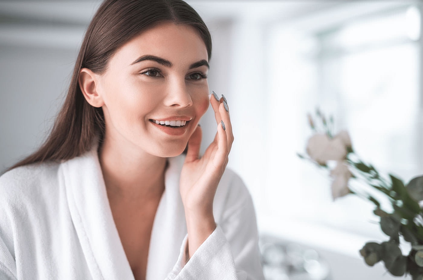 Woman applying skincare and smiling in bathroom.